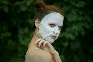 retrato de un mujer toques su hombro con su mano blanco máscara piel cuidado arbustos en el antecedentes foto