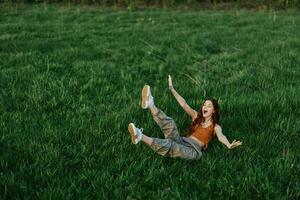 Young woman playing games in the park on the green grass spreading her arms and legs in different directions falling and smiling in the sunlight of summer, a lifestyle of life and youth photo