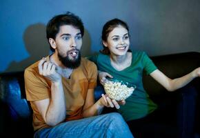 amigos hombre y mujer acecho televisión en el sofá y palomitas de maiz en un plato foto