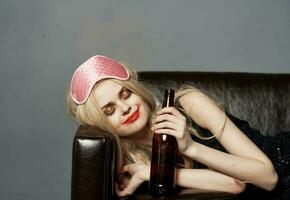 A woman with a pink mask on her head and a bottle of beer sleeps on the couch photo