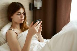 mujer con móvil teléfono mentiras en cama cerca ventana y cortinas diseño foto