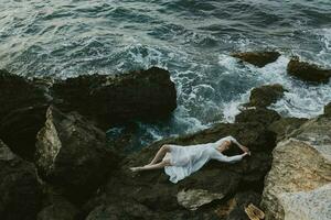 woman in long white dress wet hair lying on a rocky cliff view from above photo