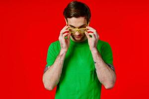 a man in a green t-shirt with tattoos in his hands wearing glasses on a red background photo