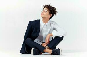 curly-haired guy in fashionable clothes and sneakers sits on the floor in a bright room in full growth photo