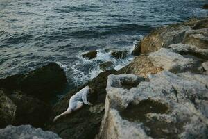 Beautiful bride lying on rocky coast with cracks on rocky surface view from above photo