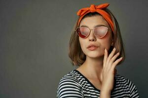 mujer vistiendo Gafas de sol en un a rayas camiseta con un vendaje en su cabeza posando Moda foto