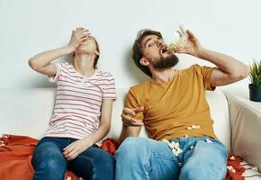 A man with popcorn in a plate and a woman are sitting on the couch watching TV and watching movies photo