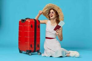 woman sitting on the floor with a red suitcase passport and plane tickets blue background photo