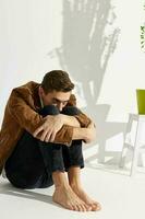 A guy in fashionable clothes sits on the floor hugging his knees with his hands photo