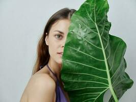 pretty woman covers half of her face with green leaf swimsuit cropped view photo