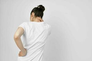 brunette in a white t-shirt pain in the neck light background photo