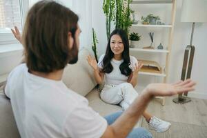 A man and a woman sit on the couch at home in white T-shirts and shouting communicate scandalously do not understand each other. A quarrel in the family of two spouses and aggression, sad emotions photo