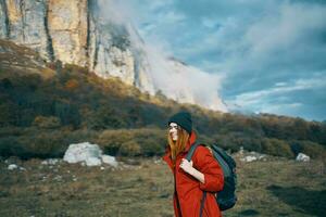 viaje de un mujer en un chaqueta con un mochila sombrero en su cabeza azul cielo y alto montañas foto
