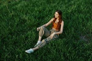 A woman relaxing on the grass in the park, wearing pants and a top and watching the sunset. The concept of relaxing without the phone and the Internet in harmony with oneself in the fresh air photo