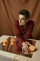 A guy in a shirt sits at a table with a mirror and orange oranges background studio photo