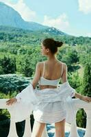 attractive young woman in a white shirt admires the green nature on the balcony sunny day photo