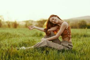 A woman sits on the green young fresh grass in the open air and laughs and smiles happily in the sunset light, her flying red hair fluttering in the wind photo