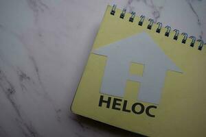 HELOC write on sticky note and house made from paper isolated on Office Desk. photo