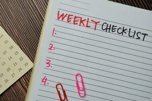 Weekly Checklist write on a book. Supported by an additional services isolated on wooden table. photo