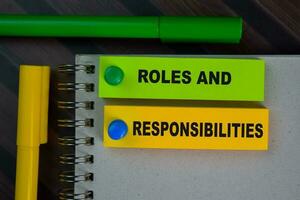 Roles and Responsibilities write on sticky notes isolated on Wooden Table. photo