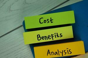 Cost Benefits Analysis write on sticky notes isolated on Wooden Table. photo