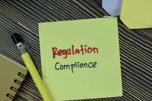 Concept of Regulation Compliance write on sticky notes isolated on Wooden Table. photo