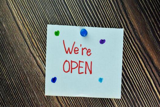 We're Open write on sticky note and isolated on Wooden Table. Business Concept photo