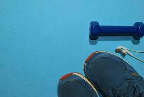blue dumbbell, sneakers and earphone indicating workout plan on blue background. Top view with copy space for any design. Healthy and fitness concept photo