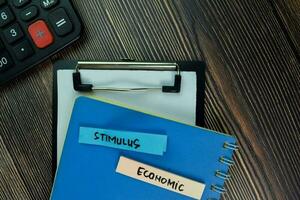 Stimulus and Economic write on sticky note and isolated on Wooden Table. Finance Concept photo