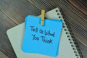 Tell Us What You Think write on sticky notes isolated on Wooden Table. photo