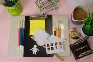 Top view of the cutting paper or drawing house on a pink table, preparing to do homework in a clipboard. Drawing Working Desk Concept photo