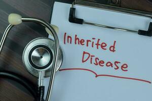 Concept of Inherited Disease write on a paperwork with stethoscope isolated on Wooden Table. photo