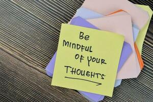 Concept of be mindful of your thoughts write on sticky notes isolated on Wooden Table. photo