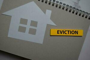 Eviction write on sticky note and house made from paper isolated on Office Desk. photo