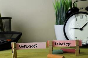 Employees and Salaries. Handwriting on sticky notes in clothes pegs on wooden office desk photo