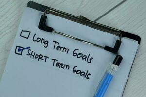 Concept of Short Term Goals write on a paperwork isolated on Wooden Table. photo