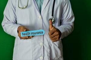 doctor standing on Green background. Hold the Health Insurance paper text. Medical and healthcare concept. photo