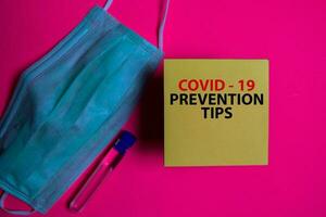 Covid - 19 Prevention Tips write on a sticky note isolated on Office Desk. Healthcare Medical concept photo