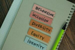 Belonging, Inclusion, Diversity, Equity, Identity write on sticky notes isolated on Wooden Table. photo