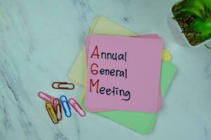 Concept of AGM - Annual General Meeting write on sticky notes isolated on Wooden Table. photo