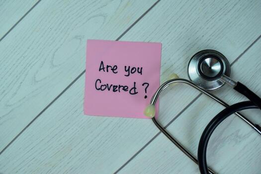 Concept of Are You Covered write on sticky notes with stethoscope isolated on Wooden Table. photo