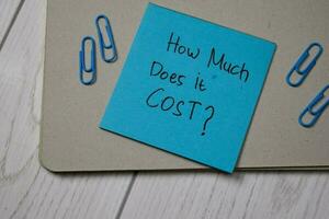 How Much Does it Cost write on sticky note isolated on wooden table. photo