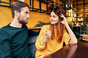 handsome man and happy woman in sweater are sitting at a table in a cafe chatting room interior photo