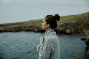 retrato de un mujer en un gris suéter soportes en un rocoso apuntalar naturaleza hembra relajante foto