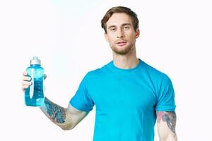 athlete in a blue t-shirt with a bottle of water on a white background and a tattoo on his arm photo