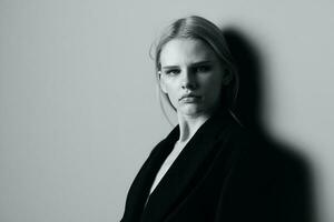 Closeup portrait of pensive serious blonde model in black jacket posing leaning on the studio wall. Stylish minimalistic shoot photo