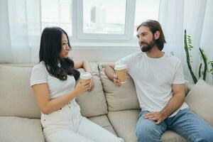 un hombre y un mujer sentado a hogar en el sofá en blanco elegante camisetas y chateando alegremente sonriente y riendo a hogar. masculino y hembra amistad foto