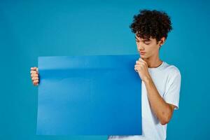 Cheerful guy with curly hair and blue mockup poster advertising photo