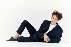 a fashionable guy in trousers and a jacket lies on the floor In a bright room, curly hair sneakers photo