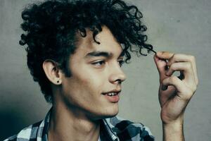 man examines his locks of hair and gray background plaid shirt handsome guy model photo